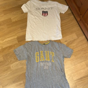 Gant T-shirt - Säljer två snygga GANT t-shirts. Ena är vit med stort GANT-tryck och sköld på bröstet, den andra är grå med gul text 'GANT East Coast 1949'. Båda har rund hals och korta ärmar, perfekta för chill dagar. Materialet känns som mjuk bomull. Storlek S/XS. 100 kr eller en för 60. Skicka dm för mer bilder eller frågor