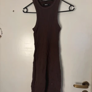 Brun ärmlös kortklänning från Bik Bok - Säljer en brun, tight och ärmlös kortklänning från Bik Bok. Klänningen har en rund halsringning och är gjord i mjuk bomull som sitter skönt mot kroppen. Perfekt för dig som gillar minimalistisk stil och vill ha en enkel men snygg look.