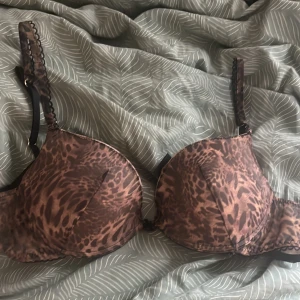 Leopardmönstrad bh-topp med vaddering - Cool bh-topp med leopardmönster i bruna och svarta toner. Vadderade kupor och justerbara axelband med dekorativ kant. Stängs med flera hyskor bak för perfekt passform. Knappt använd från intimissimi, passar 75B och 75C.
