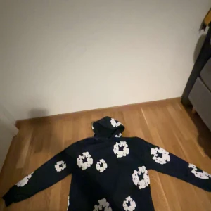 Denim Tears mjukisbyxor med blommor - Mörkblå mjukisbyxor från Denim Tears med vita blommiga tryck över hela byxorna. Byxorna har resår och snörning i midjan samt muddar vid bensluten. Perfekta för en chill och avslappnad stil.