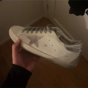 Golden goose - Snygga vita sneakers från Golden Goose med en ikonisk stjärndetalj i silver på sidan. Skorna har en klassisk snörning och en bekväm passform. Perfekta för en stilren look.