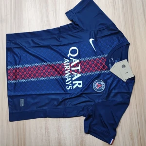 PSG matchtröja Nike marinblå S - Paris Saint-Germain fotbollströja från Nike i marinblått med korta ärmar. Tröjan har ett geometriskt mönster i blått och rött längs mitten, PSG-logga på bröstet och Qatar Airways-tryck. Tillverkad i lätt Dri-FIT polyester som andas. Perfekt för dig som älskar fotboll och PSG.