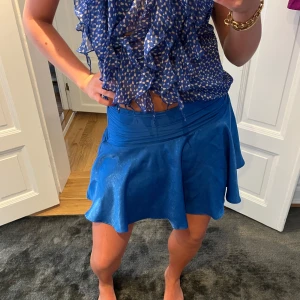 Blå kortkjol med dragkedja - Supersnygg blå kortkjol med lätt utsvängd form och markerad midja. Kjolen har en diskret dragkedja bak och ett glansigt tyg som ger en cool look. 