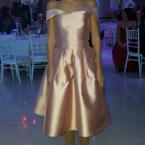 Rosa offshoulder kortklänning - Superfin kortklänning i rosa satin med offshoulder och v-ringad hals. Kjolen är voluminös med veck och ger en elegant siluett. Perfekt för bröllop, fest och högtider. Köpt för vuxna men men insydd att passa en 10 åring (storlek 146)