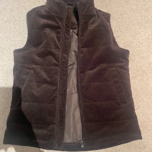 Brun manchesterväst från John Henric - Säljer en brun manchesterväst från John Henric i modellen Evora. Västen har hög krage, två sidofickor och stängs med dragkedja. Perfekt för lager-på-lager och ger en snygg, stilren look. Använd fåtal gånger. Kom pm för frågor.