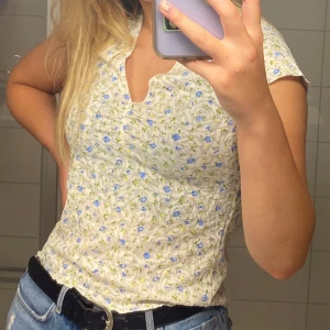 Blommig v-ringad blus från Boohoo - Supersöt blommig blus från Boohoo i ljus färg med små blå och gula blommor. V-ringad med korta ärmar och lätt rynkning vid bysten. Perfekt för dig som gillar romantisk och feminin stil.