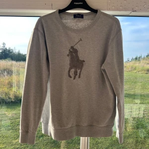 Ralph lauren tröja - Snygg grå sweatshirt från Polo Ralph Lauren med klassiskt stort broderat polospelar-motiv på bröstet. Tröjan har rund halsringning och långa ärmar, perfekt för en chill och stilren look. Mjuk och skön bomullsblandning. Skulle säga att tröjan passar mellan s-m