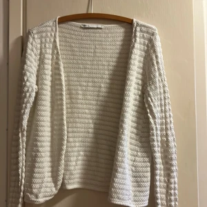 Vit stickad kofta från ONLY LIFE - Säljer en vit stickad kofta från ONLY LIFE i storlek L. Koftan har ett snyggt strukturerat mönster med lång ärm och öppen front. Perfekt att slänga över en topp för en chill och fräsch look. 