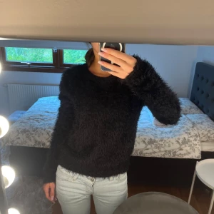 Svart fluffig stickad tröja - Mysig svart stickad tröja med fluffig textur och rund hals. Långärmad modell som är perfekt för kyligare dagar. Enkel och stilren design som är lätt att matcha med olika outfits.