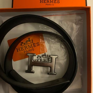 Blått bälte med H-spänne - Säljer ett blått skärp med klassiskt stort H-spänne i silverfärgad metall. Du får med innehållet och boxen.