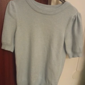 Ljusblå stickad tröja från Vila S - Supersöt ljusblå stickad tröja från Vila med korta puffärmar och bred ribbad kant vid halsen. Perfekt för dig som gillar en enkel men ändå trendig look. Mjuk och skön, passar till både jeans och kjol.