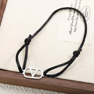 Svart armband med silverdetalj - Snyggt svart armband med justerbar snörning och en stilren silverfärgad detalj i mitten med V-formad design. Perfekt för dig som gillar minimalistiska accessoarer och vill ha något som passar till allt.