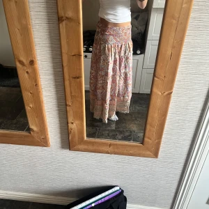 Bohemisk kortklänning med blommigt mönster - Säljer en bohemisk kortklänning med blommigt mönster i ljusa toner av beige, rosa och orange. Klänningen har smock upptill och volangdetaljer nedtill, perfekt för sommarens alla tillfällen. Materialet känns lätt och luftigt, och modellen är offshoulder.