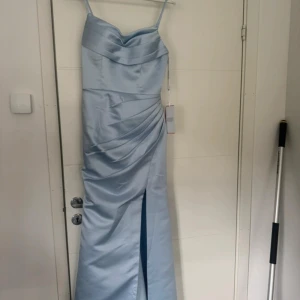 Ljusblå långklänning (Balklänning) - Elegant ljusblå långklänning i satin från JJ's House. Klänningen har smala axelband, draperad överdel och en snygg slits framtill. Materialet är glansigt och ger en lyxig känsla, perfekt för speciella tillfällen. Storlek 36. orginal pris 1445kr + typ 300kr i frakt 🌸💕