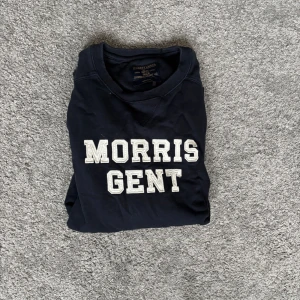 Morris Gent mörkblå sweatshirt M - Mörkblå sweatshirt från Morris Gent med vit broderad text på bröstet. Klassisk rund halsringning, ribbade muddar och lång ärm. Perfekt för en chill och stilren look. Tillverkad i mjuk bomull för skön komfort.