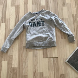 Grå sweatshirt från GANT XS - Snygg grå sweatshirt från GANT i storlek XS med trycket 'NEW HAVEN GANT' på bröstet. Tröjan har rund hals, långa ärmar och ribbade muddar. Perfekt för en chill och sportig look. Mjuk insida i bomullsmix.