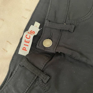 Svarta skinny byxor från Pieces - Svarta byxor från Pieces med skinny passform och klassisk femficksdesign. Byxorna har hällor för bälte, knapp och dragkedja framtill. Snygga och stilrena, perfekta till många olika looks.