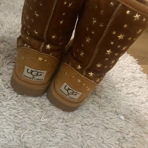Bruna UGG & Jimmy Choo boots med stjärnor - Snygga bruna boots från UGG & Jimmy Choo med glittriga stjärnor över hela ytan. Perfekta för att ge en touch av glamour till din vintergarderob. De har en klassisk UGG-design med en bekväm passform. Och ifall man inte gillar detaljen med stjärnor så kan man peta bort dom så blir det som helt vanliga basic uggs. Nästan helt oanvända. Storlek 36/37 skulle passa 38 också misstänker jag🥰 Äkta uggs och rör sig mot 2500 kronor om inte mer. Är helt öppen mot prisförslag så bara att skriva!