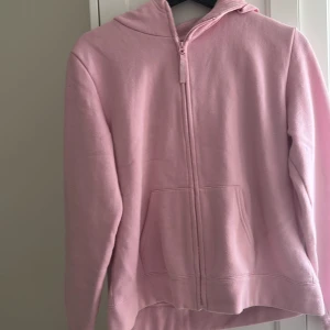 Rosa hoodie med dragkedja - Säljer en mysig rosa hoodie med dragkedja och huva. Perfekt för kyliga dagar. Den har en praktisk ficka framtill och långa ärmar.