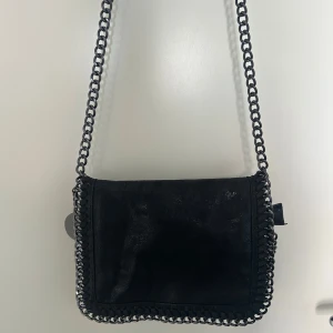 Svart axelväska med kedjedetaljer - Snygg svart axelväska med kedjedetaljer runt kanterna. Väskan har en stilren design och är perfekt till din outfit. Passar till allt. Den har en praktisk storlek för att bära dina nödvändigheter.