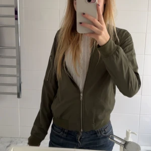 Olivgrön bomberjacka från Vero Moda - Säljer en snygg olivgrön bomberjacka från Vero Moda. Jackan har dragkedja framtill och ribbade muddar vid ärmslut och nederkant. Tunnare i materialet och jätteskön