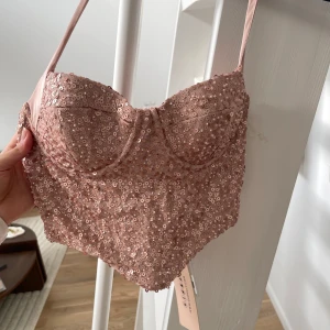 Rosa paljettprydd korsett från Oh Polly - Säljer en snygg rosa korsett från Oh Polly, täckt med glittrande paljetter. Den har smala axelband och en dragkedja i sidan för enkel påklädning. Perfekt för att glamma upp vilken outfit som helst! ✨