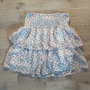Blommig kjol från Vero Moda - Charmig blommig kjol från Vero Moda i vitt med små rosa och gröna blommor. Kjolen har en volangdetalj och en elastisk midja för en bekväm passform. Perfekt för sommarens varma dagar.💞💞