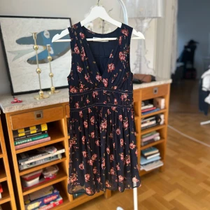 Blommig klänning från Abercrombie & Fitch - Säljer en snygg blommig klänning från Abercrombie & Fitch i mörkblått med röda och rosa blommor. Klänningen har en v-ringad design och är ärmlös, perfekt för sommarens varma dagar. Aria Montgomery/PLL vibes.