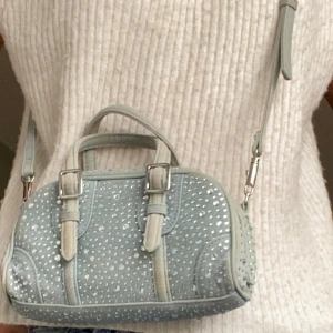 Glittrig axelväska i jeansmaterial - Snygg axelväska i ljusblått jeansmaterial med glittriga detaljer. Väskan har en dragkedja upptill och justerbar axelrem. Jättefin till våren och sommaren! 🩵 
