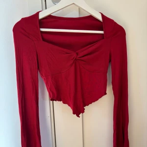 Röd långärmad croppad topp från SHEIN  - Snygg röd långärmad topp med en twistdetalj framtill och croppad design. Perfekt för att ge en trendig touch till din outfit.