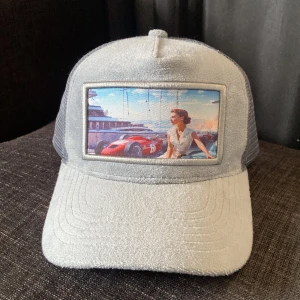 Grå keps med retrotryck - Snygg grå keps från Revenite med ett coolt retrotryck på framsidan. Kepsen har ett nätmaterial på baksidan för extra ventilation och en justerbar rem för perfekt passform.