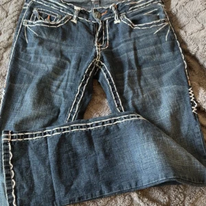 Blå jeans med broderade fickor - Snygga blå jeans med unika broderade detaljer på bakfickorna. Byxorna har en normal passform och är dekorerade med kontrasterande sömmar. W:28 L:34 jag är runt 164, dom är lowrise och formar kroppen jätte fint!