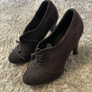 Svarta mocka pumps med snörning - Snygga svarta pumps i mocka med snörning framtill. De har en elegant klack och en spetsig tå, vilket ger en stilren look. Perfekta för att lyfta vilken outfit som helst. Snörena är sönder och har knutits ihopa men det går lätt att fixa igen med nya snören🖤