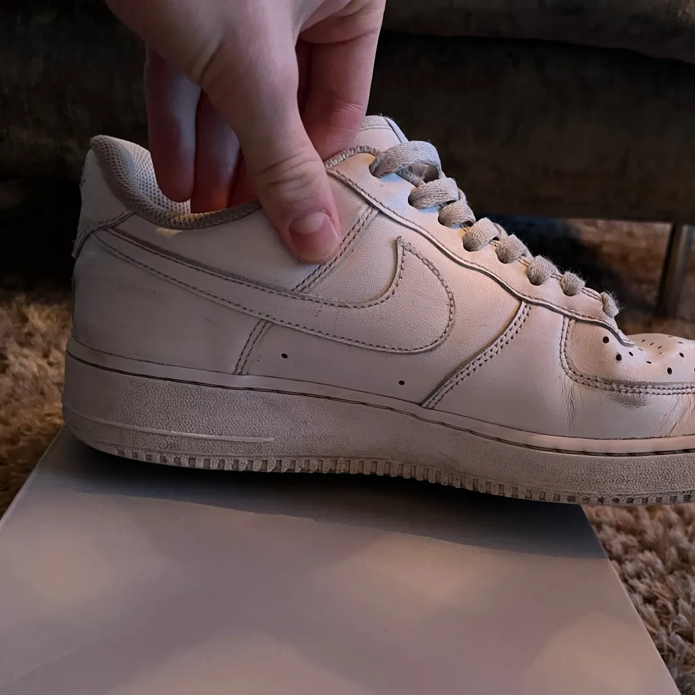 Säljer ett par klassiska vita Nike Air Force 1 '07. Skorna har en stilren design med snörning och perforerade detaljer på tån för ventilation. Perfekta för en casual look. Man får med ett par skydd till framsidan av skon också. Kengät.
