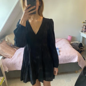 Svart klänning från Zara - Snygg svart klänning från Zara med v-ringning och broderade detaljer. Klänningen har långa ärmar och en kort, verkligen super fin! Helt nytt skick men ursäkta för lite katthår på bilderna, rollar den självklart innan köp😁💓