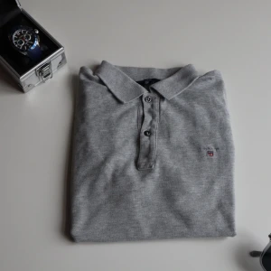  pikétröja från Gant - Säljer en  grå pikétröja från Gant med klassisk krage och knappslå. Tröjan har en liten broderad logotyp på bröstet och korta ärmar. Perfekt för en avslappnad look orginal pris 589 säljer för 289