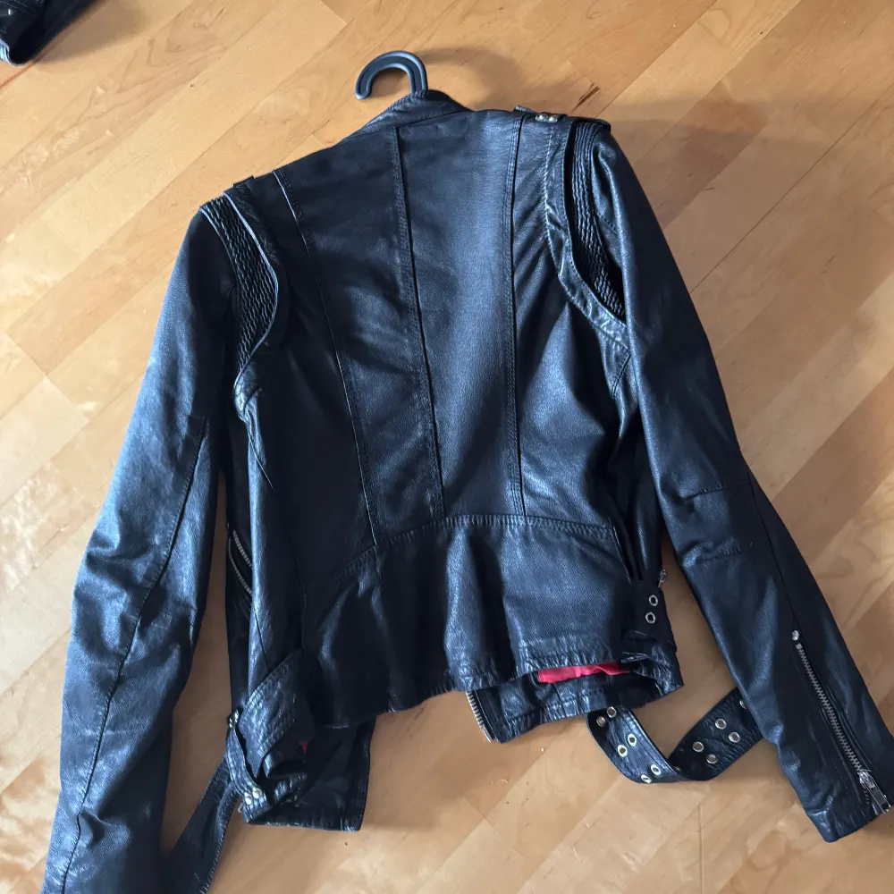 Snygg svart skinnjacka från Jofama med coola detaljer som dragkedjor och bälte. Insidan har ett rött och svart blommigt mönster. Storlek 40 men funkar för en mindre person med . Takit.