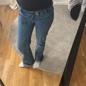 Blå jeans med dubbla knappar - Snygga blå jeans med dubbla knappar framtill och en klassisk femficksdesign. De har en rak passform och är perfekta för en avslappnad stil. Jeansen har en medelhög midja och är tillverkade i ett slitstarkt denimtyg.