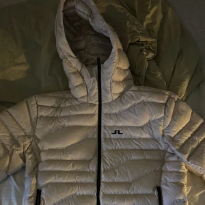 Jacka från J.Lindeberg - Säljer en stilren beige dunjacka från J.Lindeberg. Jackan har en dragkedja framtill och är långärmad med en pufferdesign. Perfekt för våren. Jackan är i nyskick och aldrig använd bara provad, skriv om ni vill ha fler bilder!