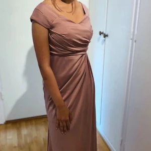 Rosa balklänning - Elegant rosa långklänning med draperad detalj framtill och korta ärmar. Perfekt för festliga tillfällen. Klänningen har en vacker passform och en dragkedja i ryggen.