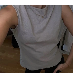 Grå ärmlös topp - Säljer en stilren grå ärmlös topp i mjukt material. Perfekt för en avslappnad look. Toppen har en rund halsringning och en enkel design som gör den lätt att matcha med olika outfits.