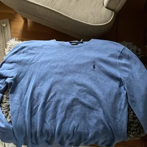 Blå tröja från Polo Ralph Lauren - Säljer en stilren blå tröja från Polo Ralph Lauren i bomull. Tröjan har en klassisk design med rund hals och långa ärmar. Perfekt för en avslappnad men ändå snygg look. Den är i nyskick. De är storlek M men den sitter som en S