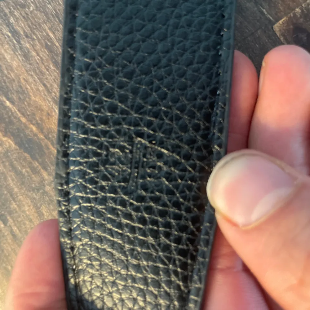Snyggt svart skärp i skinn med ett stilrent metallspänne format som ett H. Perfekt för att ge en elegant touch till din outfit. Skärpet har en slät yta med diskreta sömmar längs kanterna.. Asusteet.