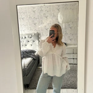 Vit blus med volang och v-ringning - Säljer en luftig vit blus med v-ringning och volangdetaljer. Blusen har långa ärmar och en lös passform, perfekt för en avslappnad men ändå stilren look. Passar till både jeans och kjol.