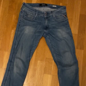 Blå Replay Anbass jeans - Säljer ett par klassiska blå Replay Anbass jeans med fem fickor och snygga slitningar. Jeansen har normal passform och raka ben, perfekt för en avslappnad stil. Märkeslapp bak i midjan och diskreta detaljer på bakfickorna.