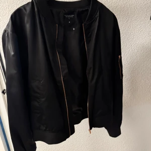 Svart bomberjacka från Lager157 - Säljer en stilren svart bomberjacka från Lager157. Jackan har klassisk passform, dragkedja framtill och ficka med dragkedja på ärmen. Perfekt för dig som vill ha en enkel och snygg jacka till vardags.