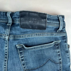 Blå jeans från Jacob Cohen - Säljer ett par klassiska blå jeans från Jacob Cohen Milano. Jeansen har normal passform, raka ben och fem fickor. Tillverkade i Italien med snygga detaljer och diskret logga på fickan. Perfekta för en stilren vardagslook.