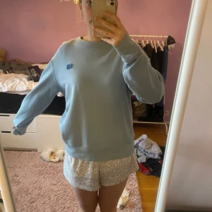 Ljusblå sweatshirt från Acne Studios - Säljer en ljusblå sweatshirt från Acne Studios med det klassiska Face-logotypen på bröstet. Tröjan har rund halsringning och långa ärmar. Bara använt en gång så i nyskick!!