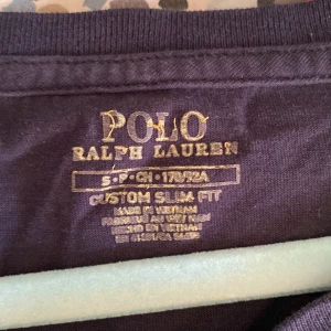Mörkblå långärmad tröja från Polo Ralph Lauren - Säljer en mörkblå långärmad tröja från Polo Ralph Lauren med röd broderad logga på bröstet. Tröjan har en slim fit passform och är tillverkad i mjuk bomull. Perfekt för en stilren och klassisk look. 