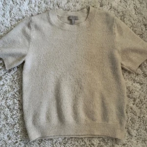 Beige stickad kortärmad tröja från H&M - Säljer en beige stickad tröja från H&M med korta ärmar och rund halsringning. Tröjan har en mjuk och lite fluffig struktur, perfekt för lager-på-lager eller sommarens svalare dagar.